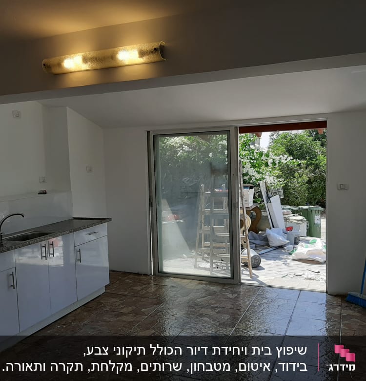 מטבח עם ארונות לבנים ודלת זכוכית לחצר